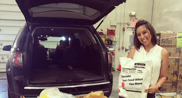 Smiling woman loading food donation bags into SUV. 