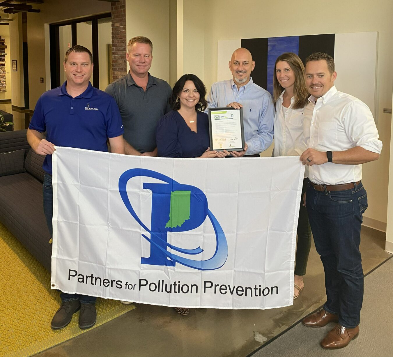 Buckingham's Director of Sustainability, and Buckingham staff, posing in front of flag that says "Partners for Pollution Prevention"