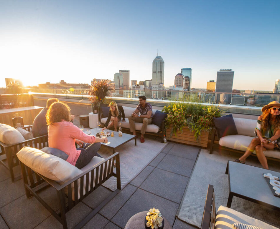 Outdoor photo of people enjoying the rooftop balcony at CityWay. The photo is at dusk with the Indianapolis Skyline in the background.